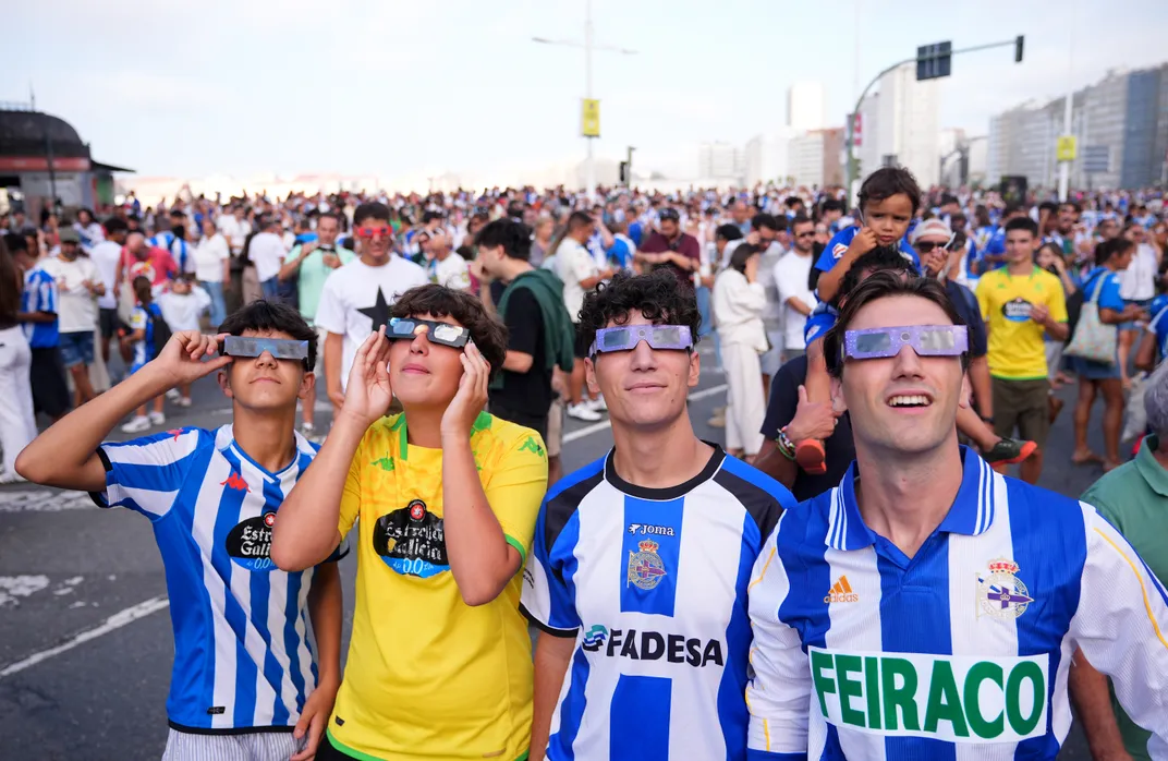 Vier junge Männer in Fußballtrikots schauen durch eine Sonnenfinsternis-Brille
