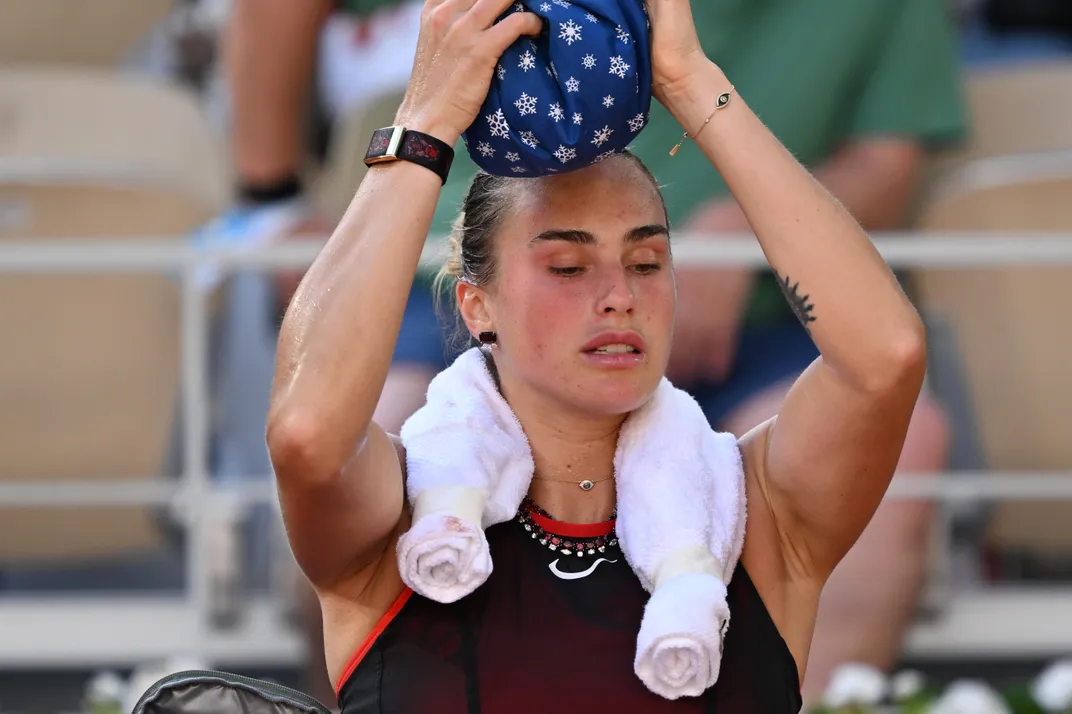 Eine Tennisspielerin legt sich einen Stoffbeutel mit Schneeflocken auf den Kopf und trägt ein kaltes Handtuch um den Hals